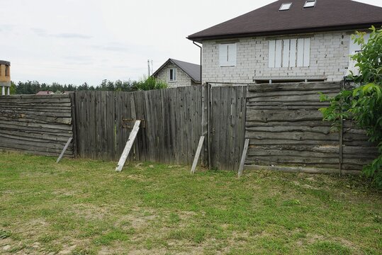 old gray wooden gate and fence wall made of boards in green grass on a rural street