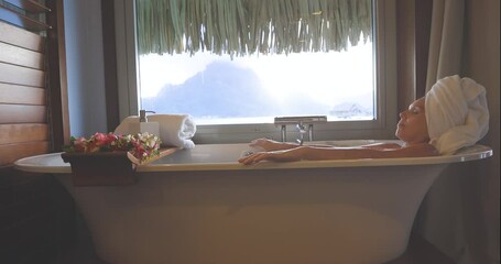 Pretty woman relaxes in a hot batch tub near a steam covered window with a mountain view. Self care spa treatment. 