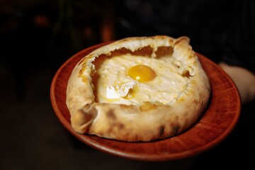 The waiter's hands in black gloves hold two traditional khachapuri with cheese and an egg