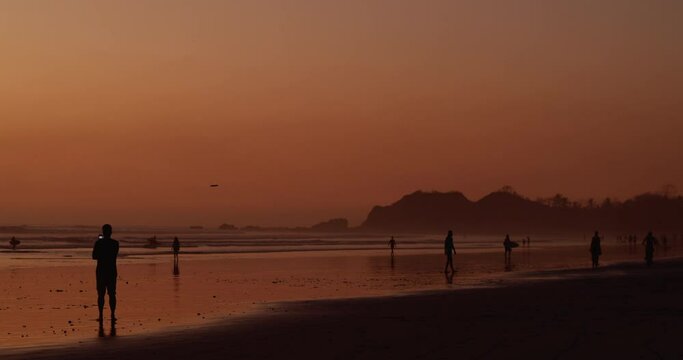 Beach goers take pictures, play frisbee and walk along beach as beautiful sun sets in the distance