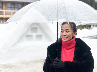 Woman tourist holding transparent umbrella in the winter and snow is falling at Shirakawago village at Gifu, Japan.