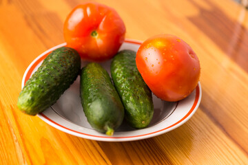 Fresh Tomatoes and Cucumbers on Plate Against Wooden Table.