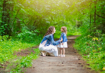 Fototapeta premium Portrait of Young Mother with Her Daughter Communicating Outdoors in green Summer Forest.