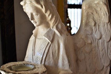 An old white statue of a winged angel holding a holy water stoup