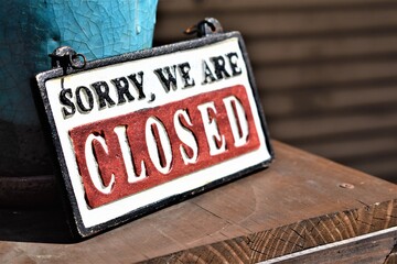 A signage that says Sorry, We Are Closed sits on top of a desk by a store window