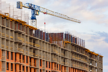 Construction of a multi-storey residential complex. Tower crane in action. Unfinished building on background of sky. Concept - work in a construction team. House is ready for installation of facade