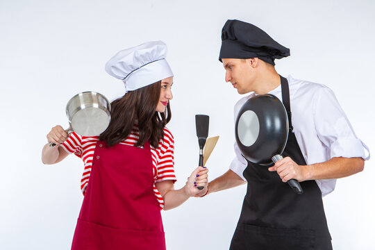 Two restaurant chef. Two cooks look at each other. Culinary battle concept. Competition of chef. Two student chefs are competing. Guy and girl in uniform of cooks. Kitchen utensils in hands of chefs