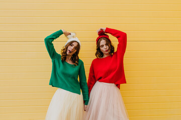 Ecstatic girls posing in knitted hats. Outdoor shot of adorable sisters holding hands.