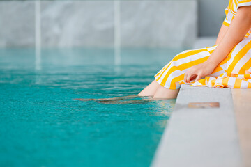 Close up Woman in yellow casual outfit resting at poolside with both feet on clear water. copy space