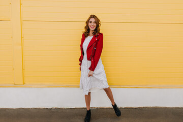 Full length photo of well-dressed girl with brown hair. Oudoor shot of young woman in red jacket.