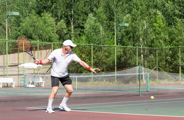 An elderly man plays tennis on an outdoor court