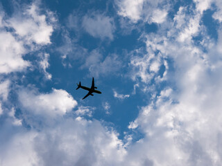 Silhouette of an airplane flying in the cloudy sky. Bottom view.