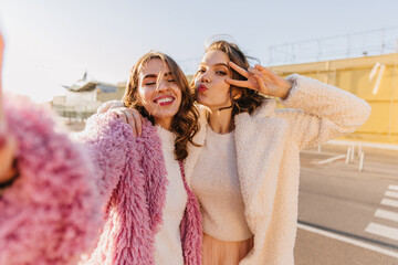 Emotional girls posing in autumn day. Outdoor shot of best friends making selfie on the street. © Look!