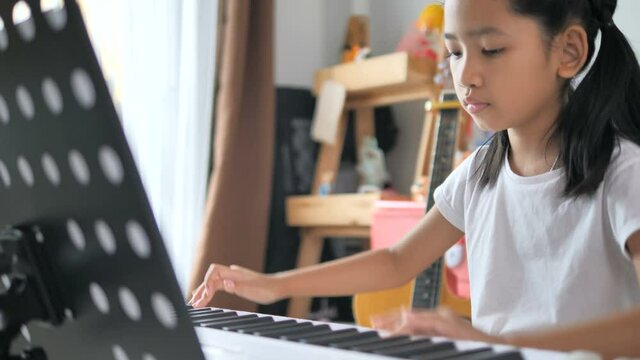 Asian little girl learning to play basic piano by using electric synthesizer keyboard for beginner music instrumental self studying at home