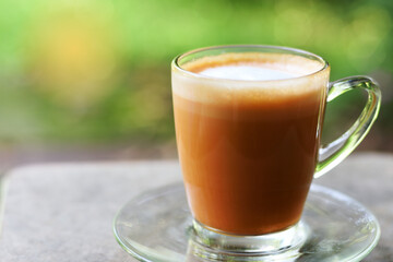 A cup of ordinary hot coffee latte with milk foam on blurred rough grey table in a peaceful morning green garden atmosphere. Beautiful time for coffee lovers.