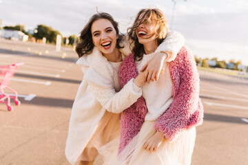 Beautiful girls in autumn coats posing on the street. Outdoor shot of two female friends laughing...