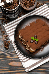 Classic tiramisu dessert and coffee grinder on ceramic plate on wooden background