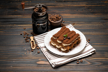 Classic tiramisu dessert and coffee grinder on ceramic plate on wooden background
