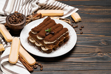 Classic tiramisu dessert on ceramic plate and savoiardi cookies on wooden background