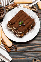 Classic tiramisu dessert on ceramic plate and savoiardi cookies on wooden background