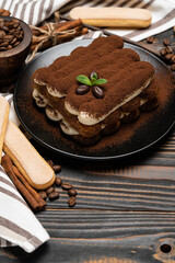 Classic tiramisu dessert on ceramic plate and savoiardi cookies on wooden background