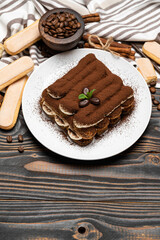 Classic tiramisu dessert on ceramic plate and savoiardi cookies on wooden background