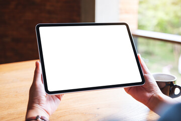 Mockup image of a woman holding digital tablet with blank white desktop screen in cafe