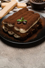 Classic tiramisu dessert and savoiardi cookies on ceramic plate on concrete background