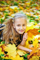 A little funny girl is lying on yellow leaves in the forest. A child on a walk in the autumn Park. Preschool girl on the street