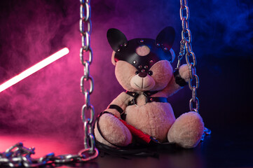 toy bear dressed in leather belts harness accessory for BDSM games on a dark background in neon light © rotozey