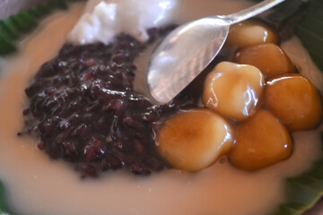 Porridge Sumsum Biji Salak, Indonesian rice flour porridge with glutinous sticky rice, served with palm sugar sauce, garnished with pandan leaves in a bowl.