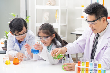 Young Asian boy and girl smile and having fun while doing science experiment in laboratory classroom with Teacher. Study with scientific equipment and tubes. Education concept.