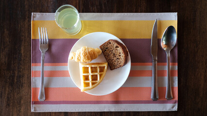 Top view breakfast with waffle, croissants and chocolate bread on white plate, spoon, knife, fork