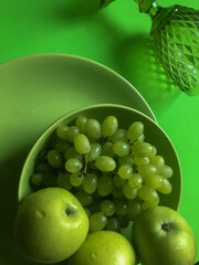 Three apples and a bunch of grapes in a green plate and a wine glass