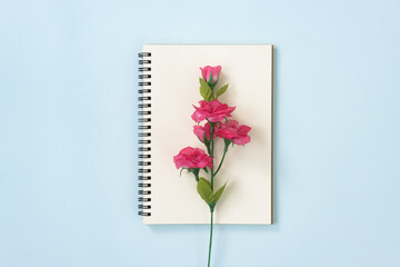 Spiral Notebook or Spring Notebook in Unlined Type and Rose Flower at Center on Blue Pastel Minimalist Background. Spiral Notebook Mockup on Center Frame