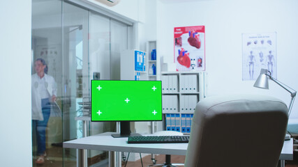 Computer with mock-up display in hospital cabinet and doctor entering in clinic. Desktop with blank and copy space green screen isolated available on display of medicine specialist in clinic cabinet.