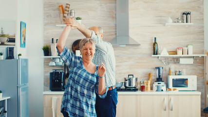 Joyful old old man and woman dancing in kitchen. Happy senior couple having fun, retired persons in cozy home enjoying life