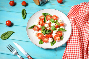 Traditional Italian Caprese Salad - sliced tomatoes, mozzarella cheese and basil on blue wooden background