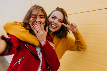 Outdoor photo of two happy female models. Carefree friends making selfie with smile.
