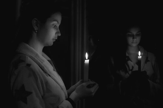Black and white girl in a dark room with a candle in her hand in front of the mirror
