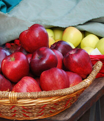 Apples of red and yellow color in wicker wooden basket. Wooden table