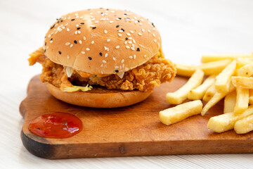 Homemade Chicken Strips Burger with French Fries and sour-sweet sauce on rustic board, side view....