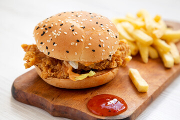 Homemade Chicken Strips Burger with French Fries and sour-sweet sauce on rustic board, side view.