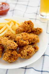 Homemade Crispy Chicken wings and French Fries with sour-sweet sauce and glass of cold beer on cloth, low angle view.