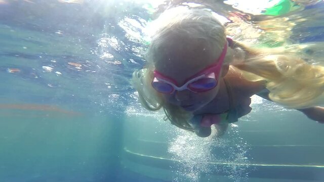 A small child swims in a pool underwater. Girl learns to swim in the pool wearing goggles for diving.