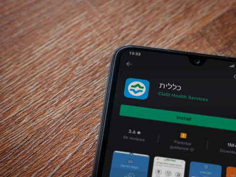 Lod, Israel - July 8, 2020: Clalit Health Services App Play Store Page On The Display Of A Black Mobile Smartphone On Wooden Background. Top View Flat Lay With Copy Space.