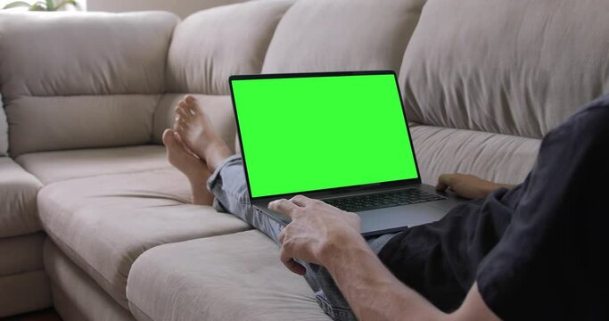 Over the shoulder shot of a man looking on pc MacBook Pro laptop green screen. Office person using laptop computer with laptop green screen staying at home
