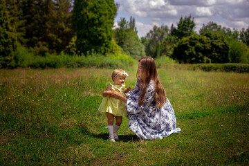 Cheerful mother plays with her little daughter at the green meadow