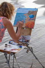 artist paints an oil painting on an easel near the sea, vertical format