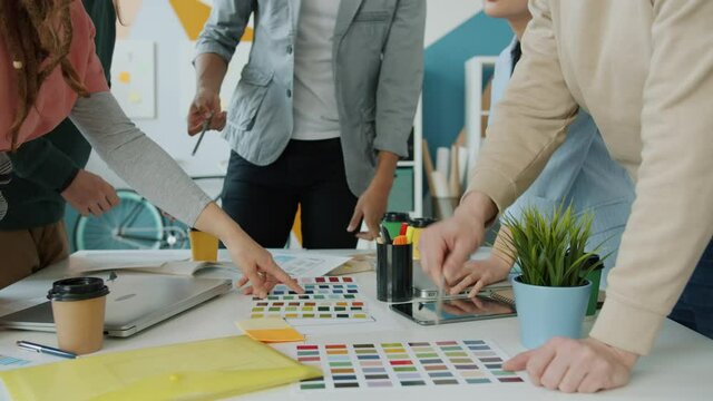 Middle shot of people designers pointing at colors during creative team meeting in office while smart phone application developers are choosing interface